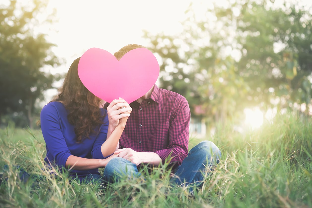 Young happy couple in love holding red paper heart in the garden. Love Romance and Valentine Concept idea.