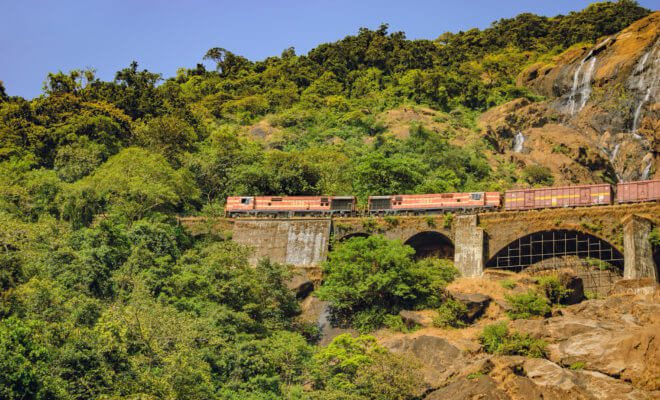 Train on the railroad bridge in the background of Dudhsagar waterfall in Goa.