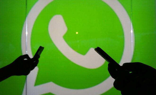 People are seen as silhouettes as they check mobile devices while standing against an illuminated wall bearing WhatsApp's logo in London in 2016.